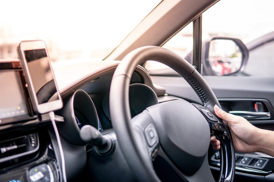 driver-hand-holding-on-steering-wheel-using-smartphone